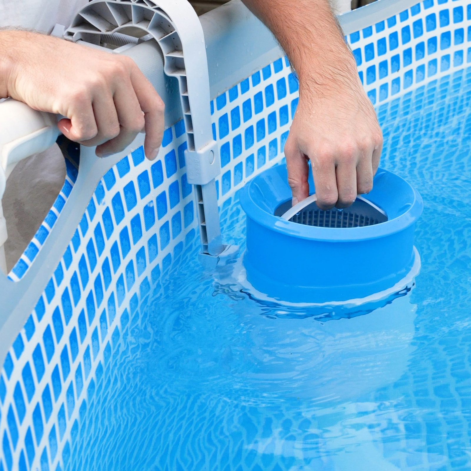 A person installs a blue pool skimmer basket inside an above-ground pool with a blue and white checkered liner, positioning the skimmer near the pool’s edge as part of Inman Pool Service’s maintenance routine.